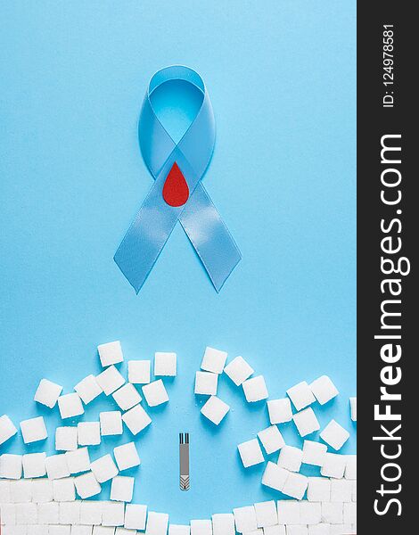 Blue ribbon awareness with red blood drop and wall made of sugar cubes ruined by Glucose Test Strips on blue background