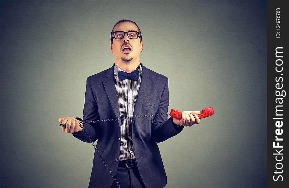 Adult frustrated businessman in suit holding red telephone receiver on gray background. Adult frustrated businessman in suit holding red telephone receiver on gray background