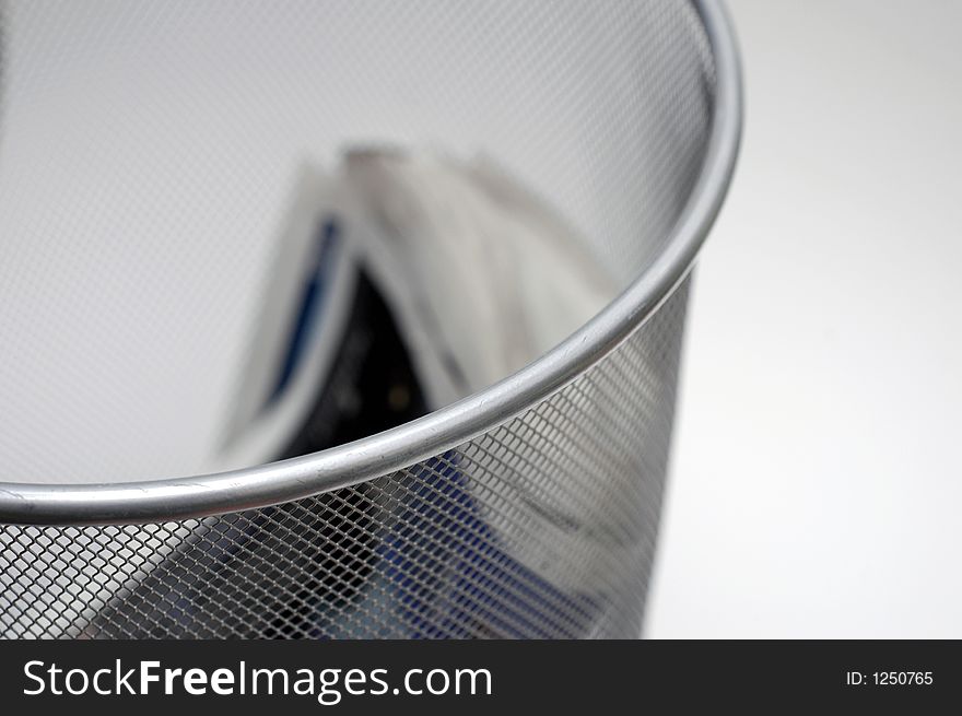 A wire waste paper basket with an out of focus discarded newspaper. A wire waste paper basket with an out of focus discarded newspaper