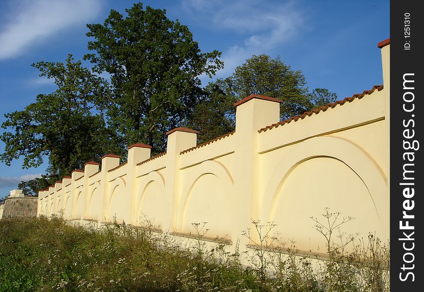 Old beige stone wall with trees and blue sky