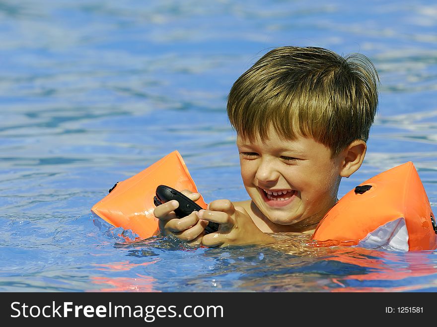 Boy child makes a call with a cell-phone in a swimming-pool. Boy child makes a call with a cell-phone in a swimming-pool