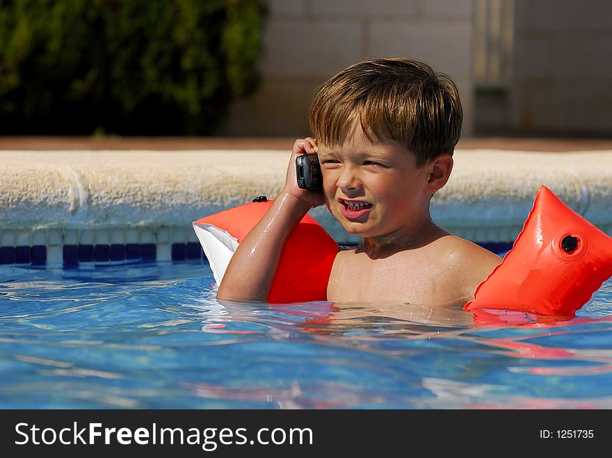 Boy child makes a call with a cell-phone in a swimming-pool. Boy child makes a call with a cell-phone in a swimming-pool