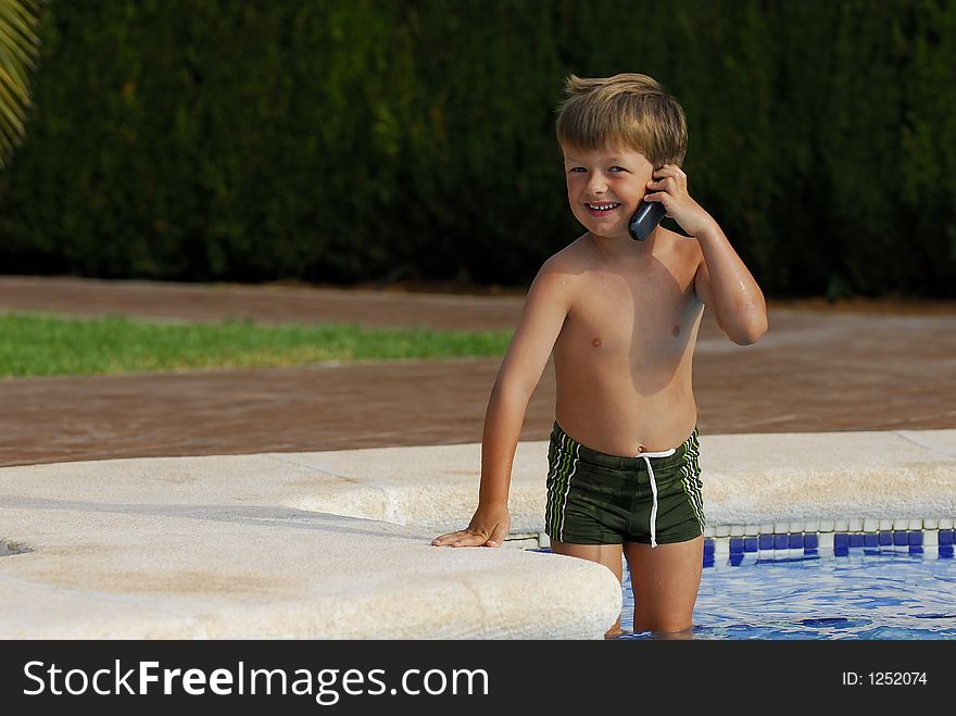 Boy child makes a call with a cell-phone standing in a swimming-pool. Boy child makes a call with a cell-phone standing in a swimming-pool
