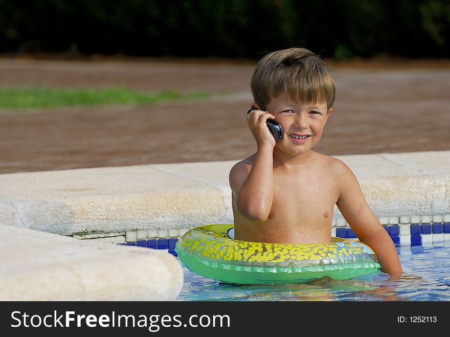 Boy child makes a call with a cell-phone sitting in a swimming-pool. Boy child makes a call with a cell-phone sitting in a swimming-pool