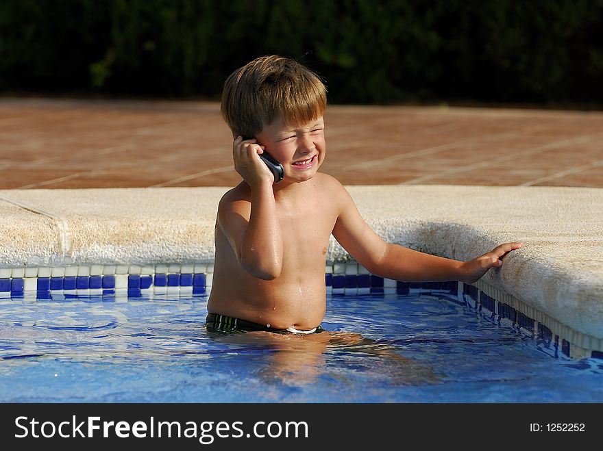 Boy child makes a call with a cell-phone sitting in a swimming-pool. Boy child makes a call with a cell-phone sitting in a swimming-pool