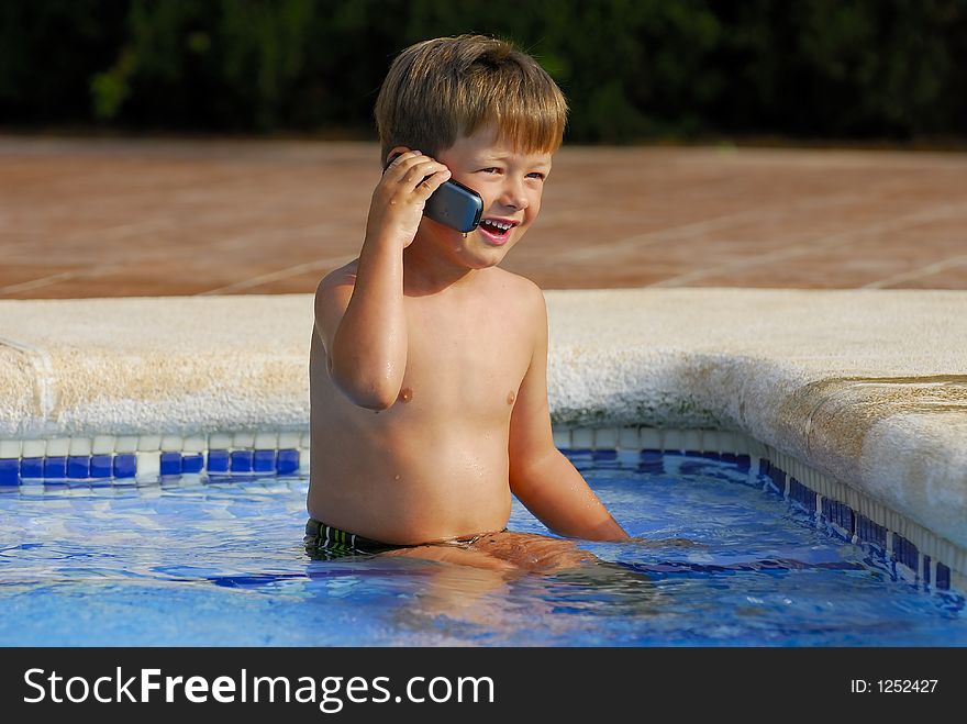 Boy child makes a call with a cell-phone sitting in a swimming-pool. Boy child makes a call with a cell-phone sitting in a swimming-pool