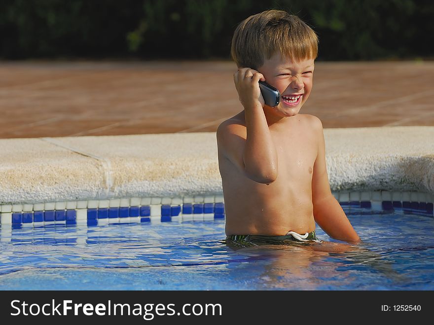 Boy child makes a call with a cell-phone sitting and laughing in a swimming-pool. Boy child makes a call with a cell-phone sitting and laughing in a swimming-pool