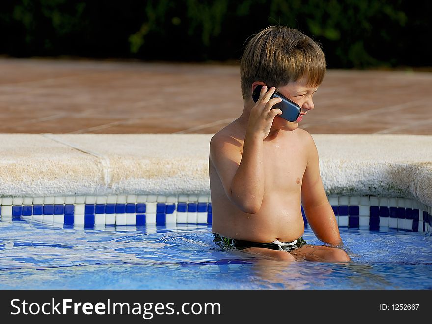 Boy child makes a call with a cell-phone sitting in a swimming-pool. Boy child makes a call with a cell-phone sitting in a swimming-pool