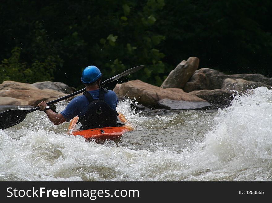 Man in blue helmet paddles kayak through whitewater. Man in blue helmet paddles kayak through whitewater