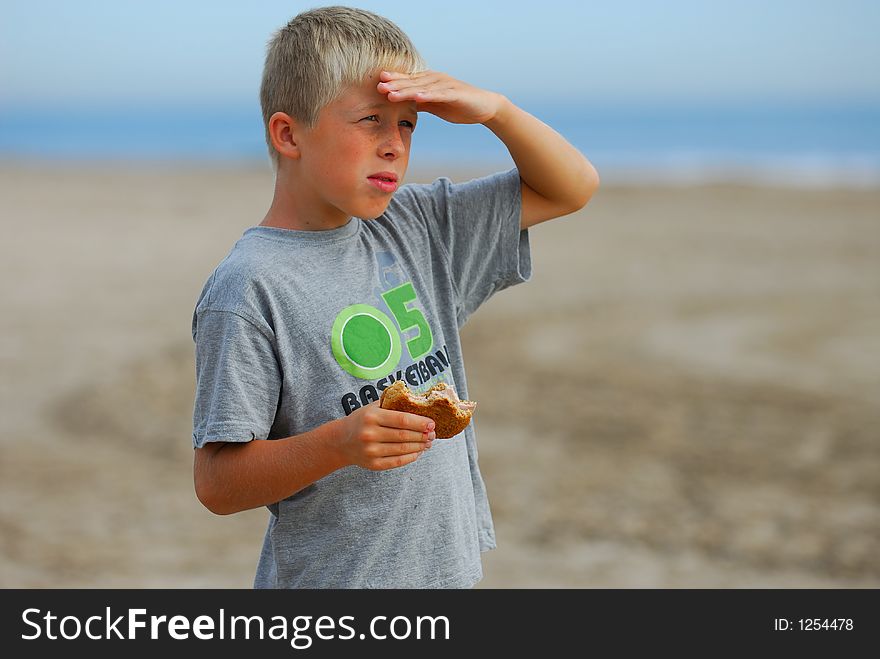 Young boy is watching the scenery at the beach and is eating a hamburger. Young boy is watching the scenery at the beach and is eating a hamburger