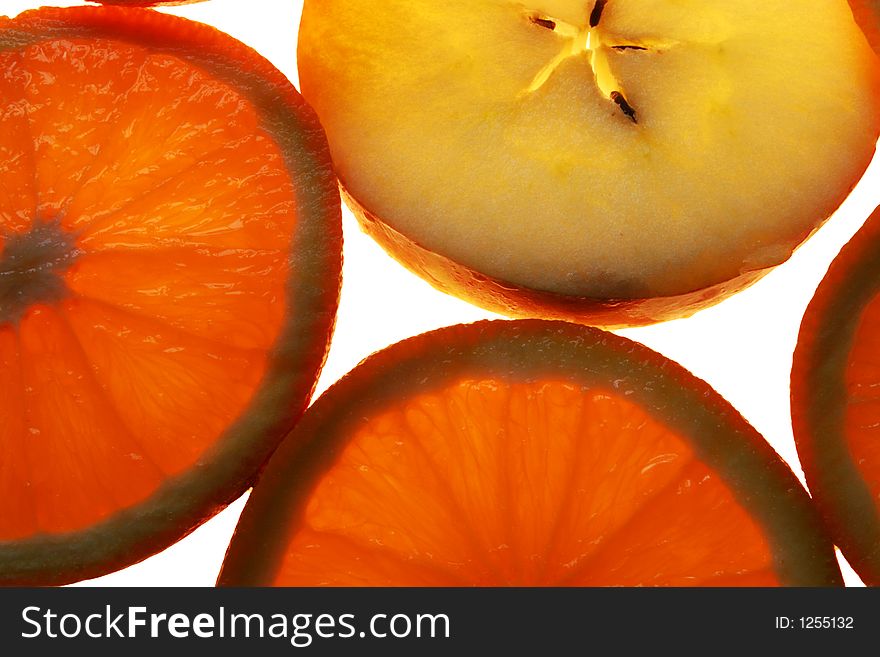 Slices of orange and apple on white background, lit from underneath. Slices of orange and apple on white background, lit from underneath