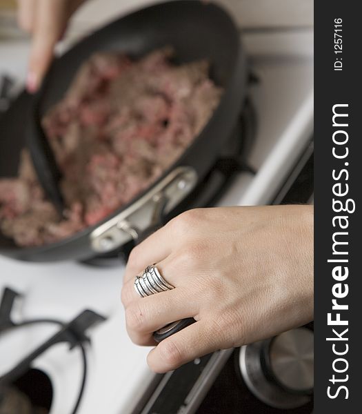 Frying meat in a pan. Narrow field of view with focus on the hand holding the pan.