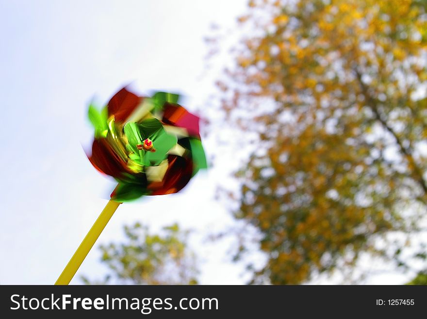 Upward view of a spinning red, yellow, and green pinwheel against white sky and orange and yellow leaves