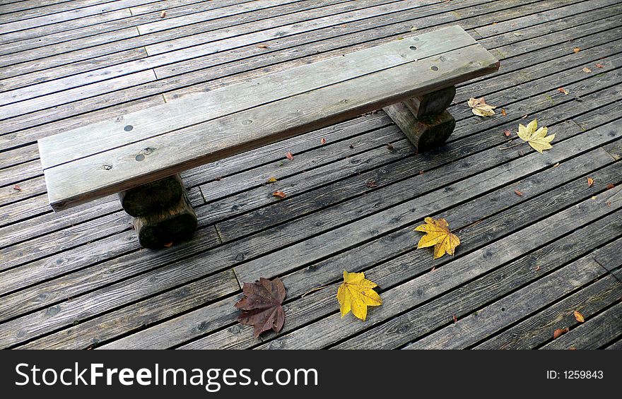 Wooden bench on the deck in the autumnal park with few yellow maple leafs. Wooden bench on the deck in the autumnal park with few yellow maple leafs