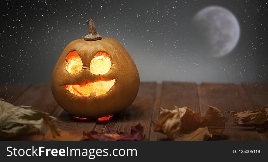 Jack o lanterns Halloween pumpkin face on wooden background and autumn leafs