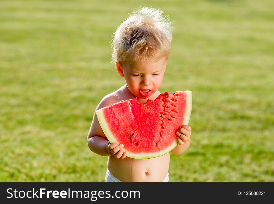 Portrait of toddler child outdoors. Rural scene with one year old baby boy eating watermelon slice in the garden. Dirty messy face of happy kid. Portrait of toddler child outdoors. Rural scene with one year old baby boy eating watermelon slice in the garden. Dirty messy face of happy kid.