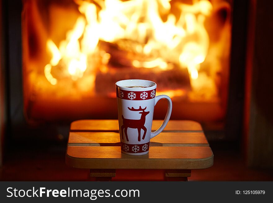 Cup of hot chocolate and marshmallows near fireplace with many candles. Cozy romantic Christmas evening