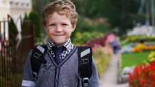 Happy Little Curly Kid Boy With Backpack Or Satchel On His First Day To School Or Nursery. Child Outdoors On Warm Sunny Stock Image