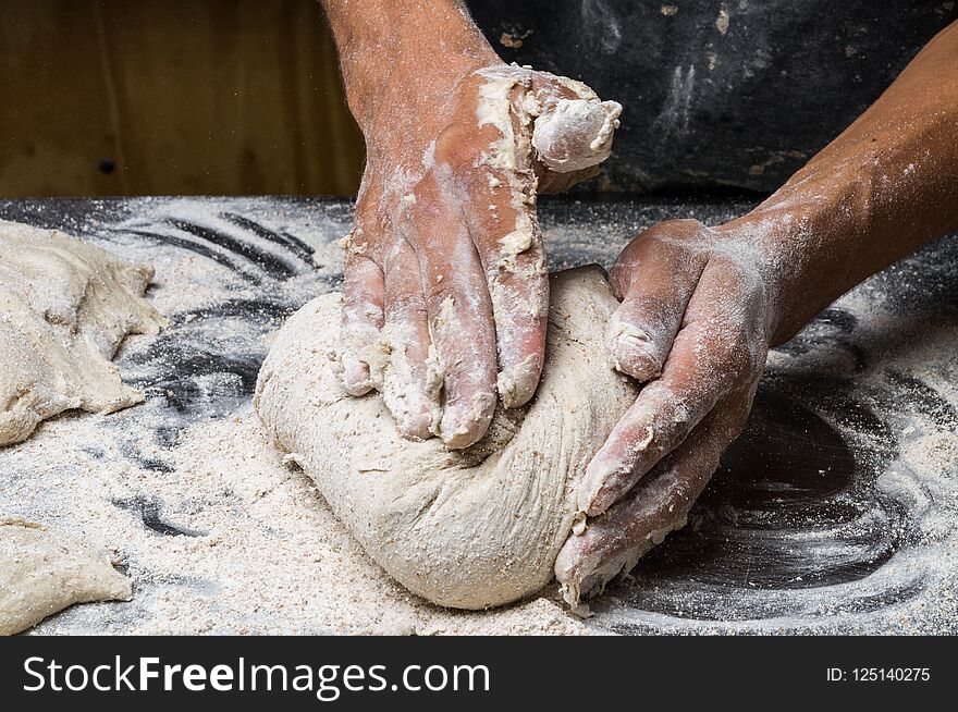 Male hands kneading dough on sprinkled with flour table, closeup