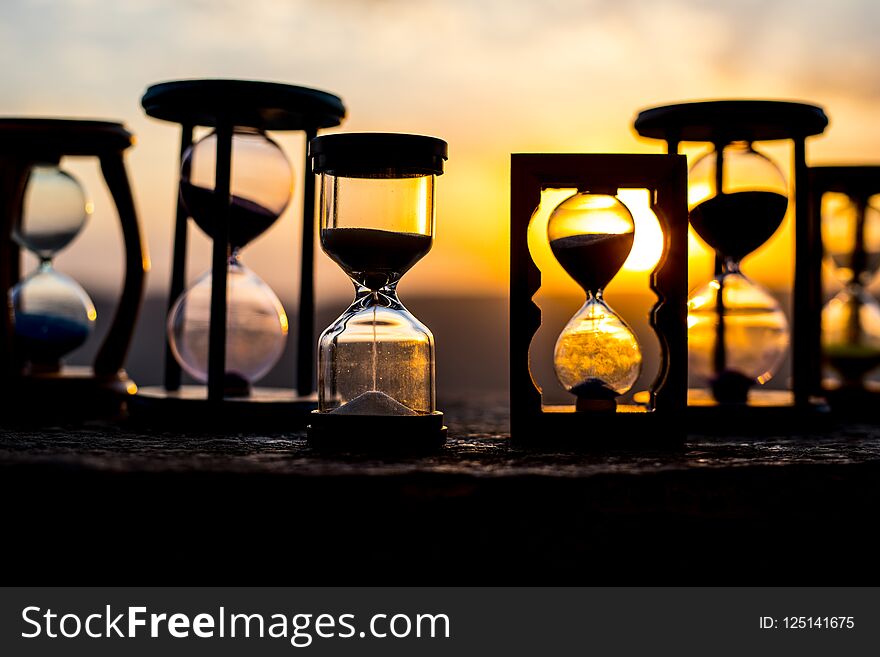 Hourglass Passing of Time Lapse Clouds. An hourglass in front of a bright blue sky with puffy white clouds passing. Time concept. Sunset time. Selective focus