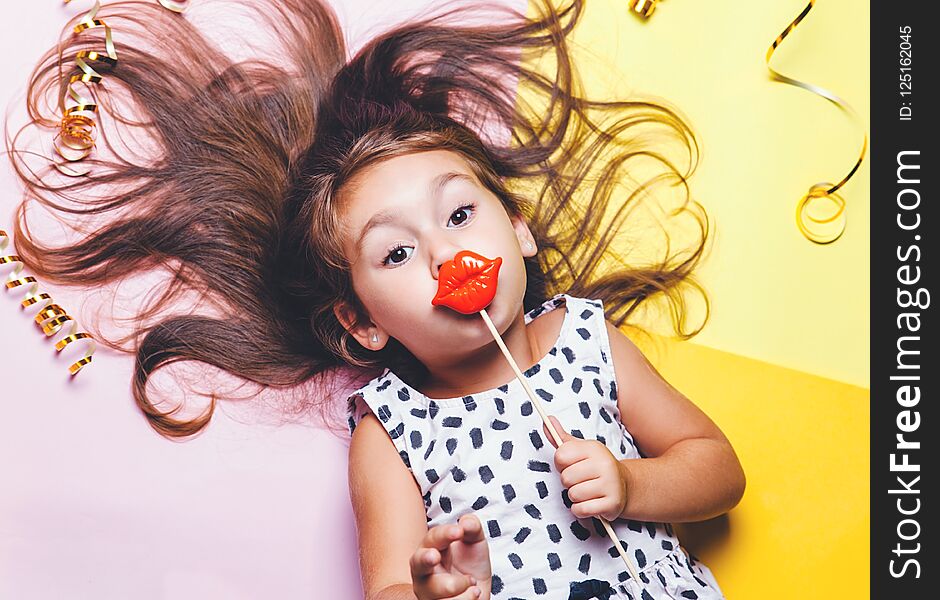 Cute little girl in funny glasses with plastic masquerade lips on stick.. Bright and festive background. Celebration masquerade portrait