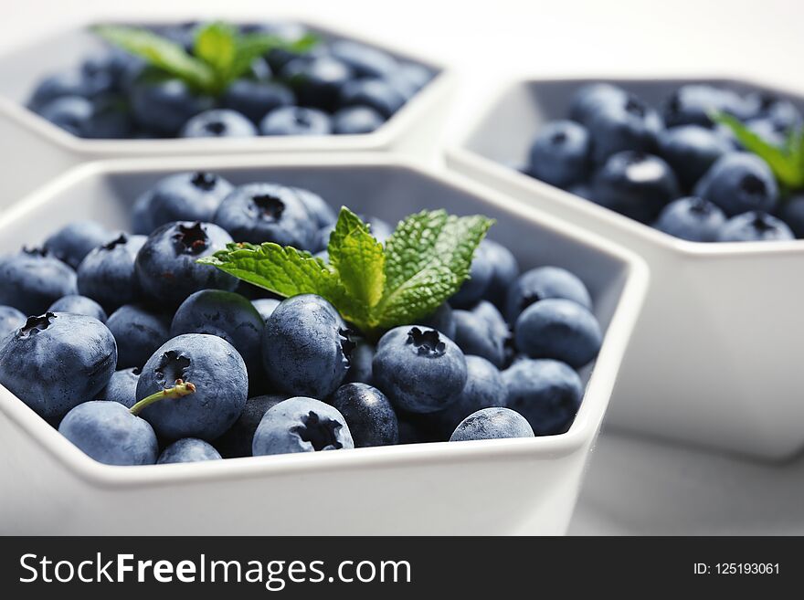 Fresh blueberries with green leaves in white dishware, closeup