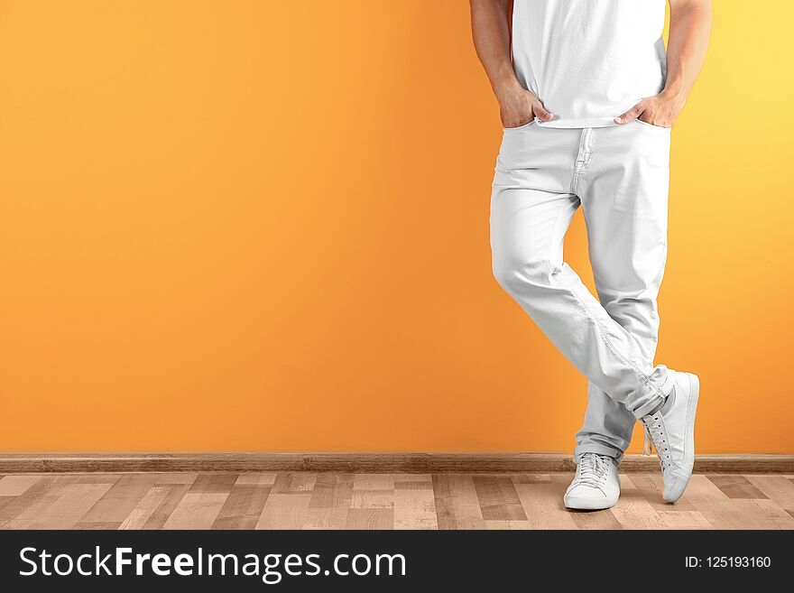 Young man in stylish jeans near color wall with space for text, focus on legs