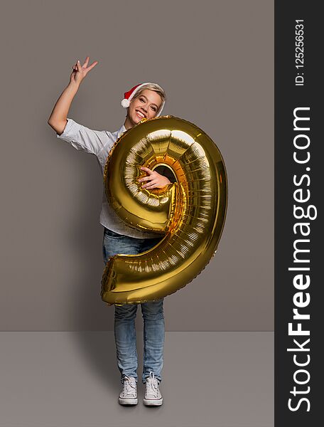 Happy girl with number 9 balloon portrait. Smiling young woman in santa hat at studio background. One of shots to compose 2018 for new year and christmas greeting card