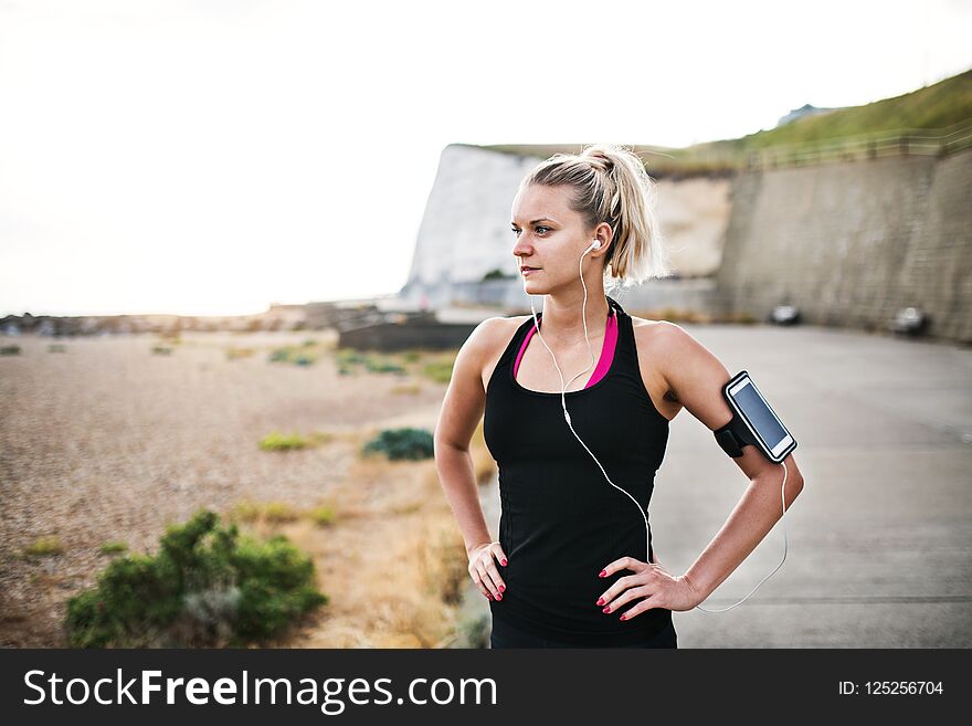 Young sporty woman runner with smartphone standing on the beach outside.