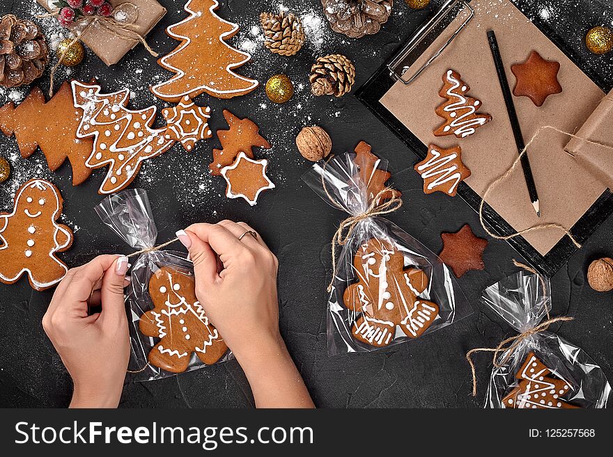 Christmas gift gingerbread on dark background. Christmas Gingerbread Cookies. Biscuits in festive packaging. Woman is packaging Christmas gingerbread cookies with icing sugar. Holiday, celebration and cooking concept. Christmas preparations concept. Top view. Christmas gift gingerbread on dark background. Christmas Gingerbread Cookies. Biscuits in festive packaging. Woman is packaging Christmas gingerbread cookies with icing sugar. Holiday, celebration and cooking concept. Christmas preparations concept. Top view