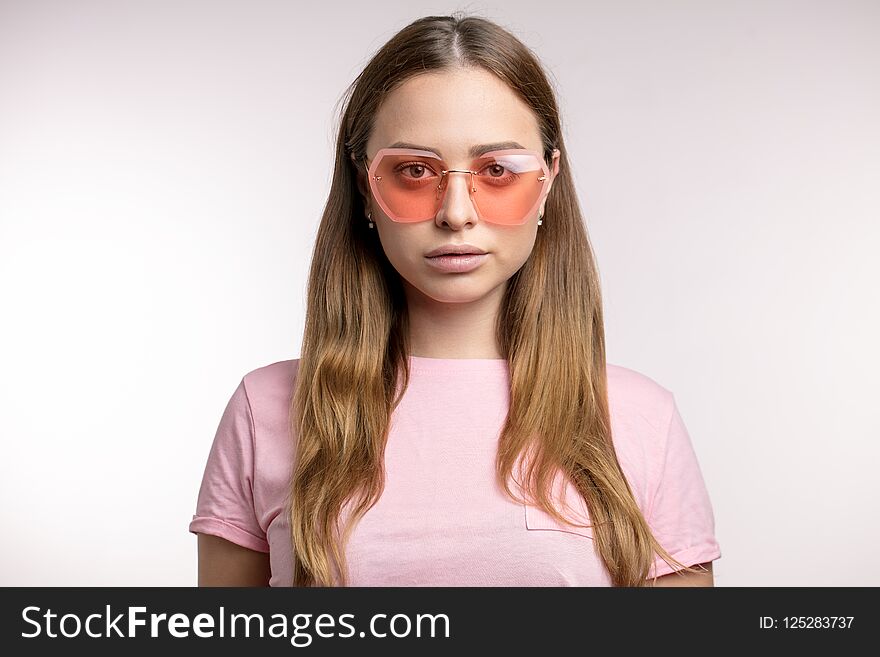 Stylish fair-haired woman looking through pink sunglasses to the camera