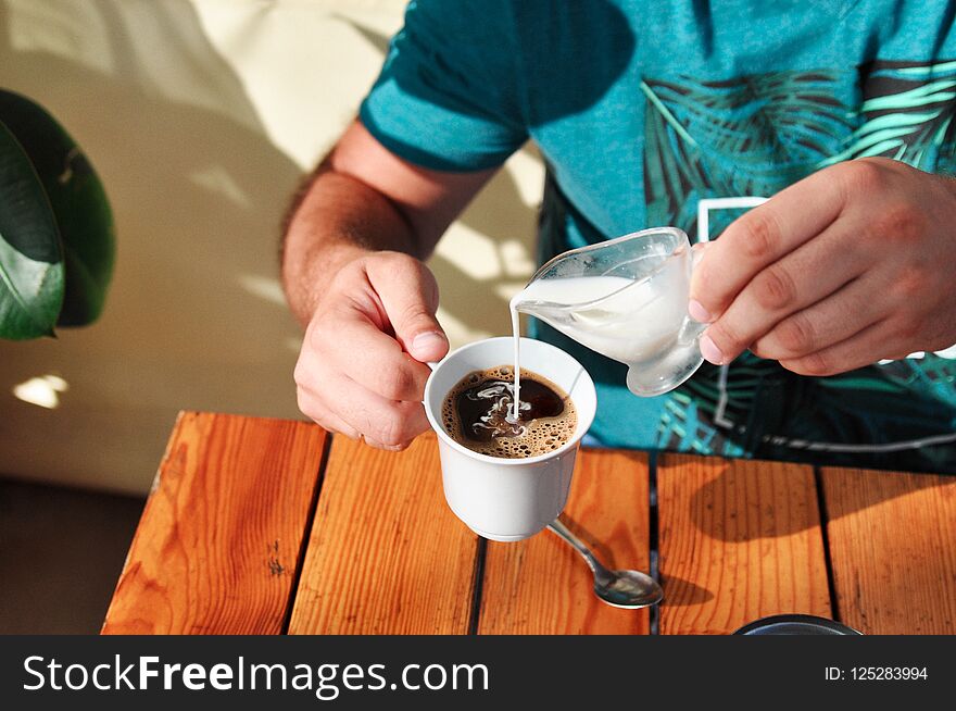 A man in a cafe pours cream into a Cup of coffee in the morning. Breakfast.