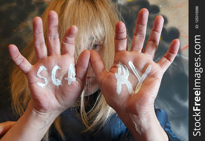 Selective focus portrait of a woman with hands in front of her face and a word Scary written on them. Selective focus portrait of a woman with hands in front of her face and a word Scary written on them