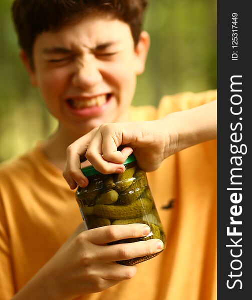 Boy with strain grimace try to remove cover from cucumbers jar