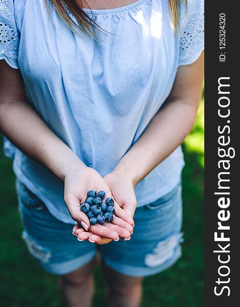 Woman holding blueberry fruits in her hands in the garden. Natural healthy foods.