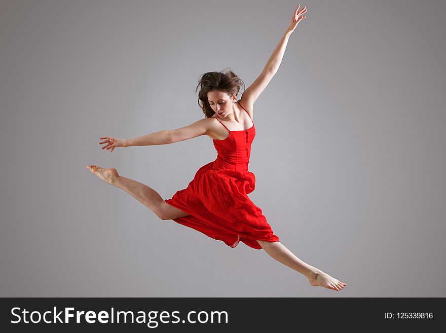 Elegant dancer in red dress jumping against gray background