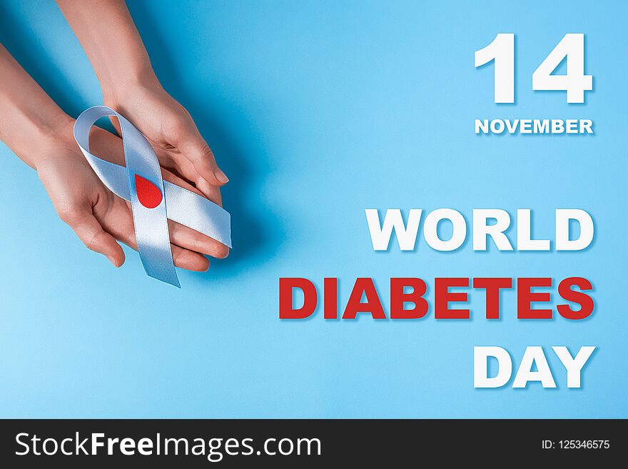 Inscription world diabetes day and blue ribbon awareness with red blood drop in woman hands on a blue background