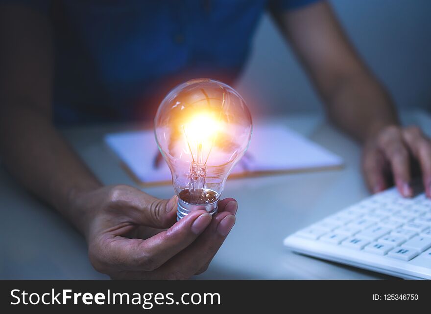 Business woman holding light bulb on the desk in office and using computer in financial,accounting,energy,idea concept.