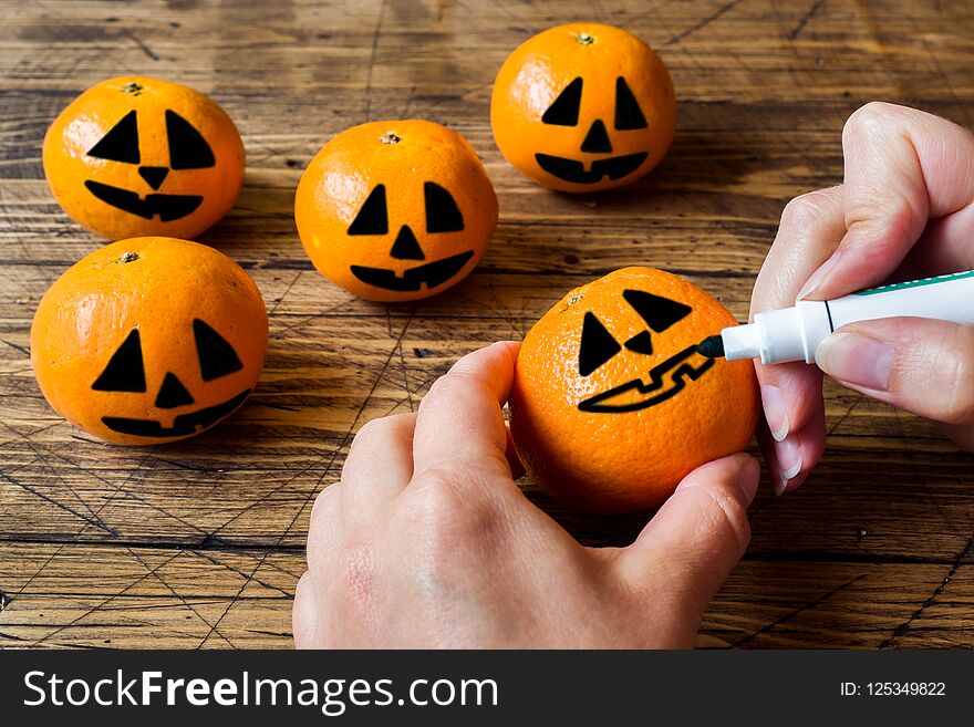 Hands draw a face on a tangerine on Halloween