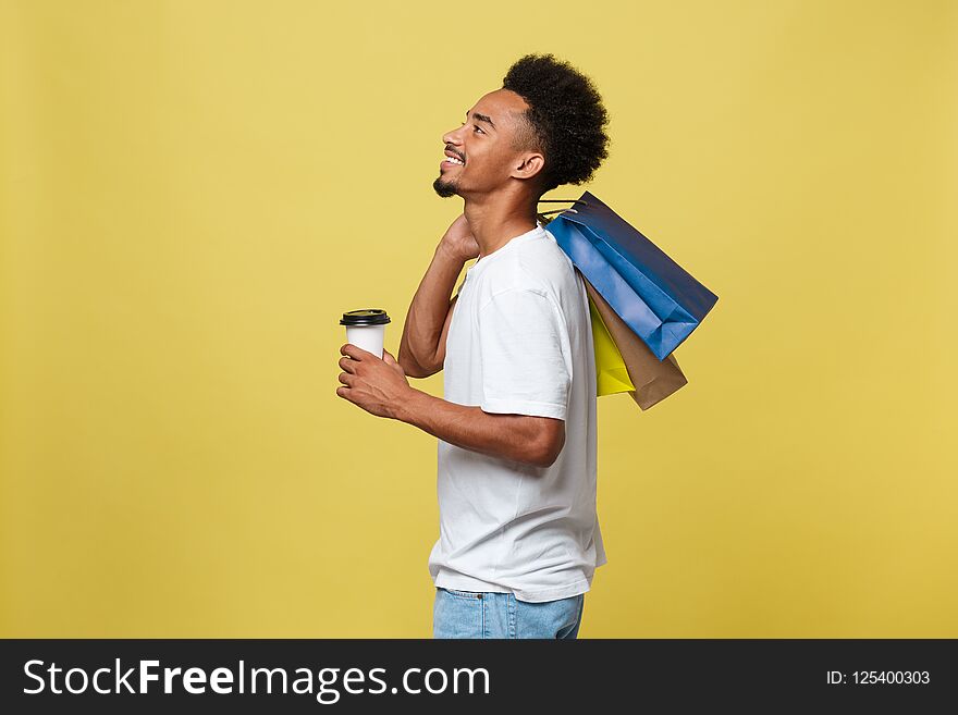 Handsome African American With Shopping Bag And Take Away Coffee Cup. Isolated Over Yellow Gold Background.