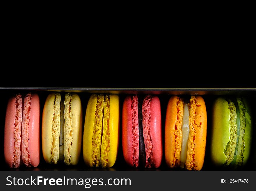 Beautiful and colorful macaroons or macarons in a box, directly above, dark background.