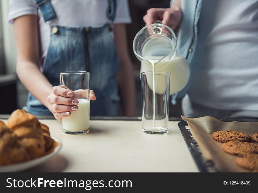 Cropped image of mom and daughter in casual clothes in kitchen at home, mom is pouring milk