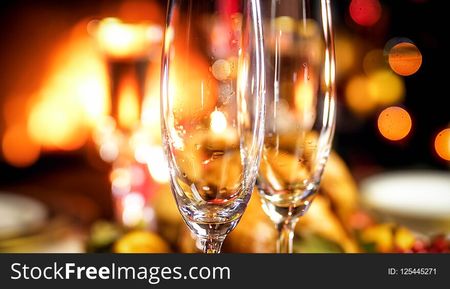 Closeup image of empty champagne glasses against burning fireplace and glowing Christmas tree