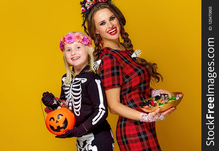 Colorful halloween. smiling modern mother and daughter in Mexican style halloween costume isolated on yellow background with Halloween candies. Colorful halloween. smiling modern mother and daughter in Mexican style halloween costume isolated on yellow background with Halloween candies