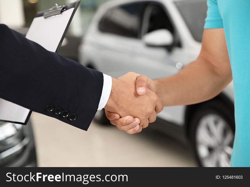 Customer and salesman shaking hands in car salon