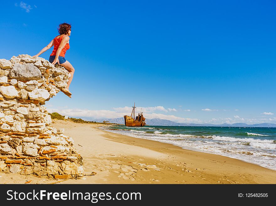 Travel freedom. Mature tourist woman on beach enjoying summer vacation. An old abandoned shipwreck, wrecked boat in the background. Travel freedom. Mature tourist woman on beach enjoying summer vacation. An old abandoned shipwreck, wrecked boat in the background