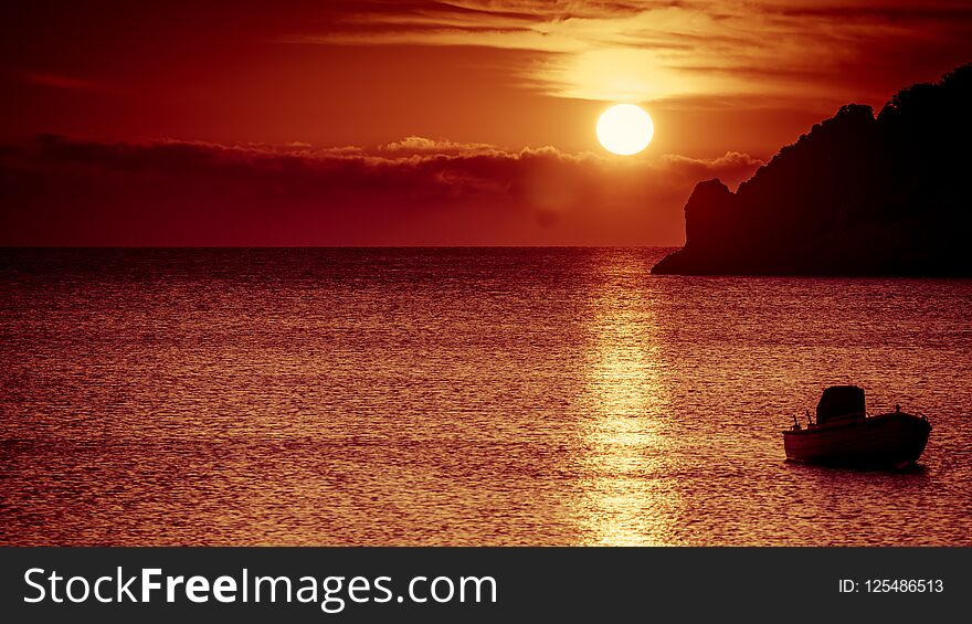 Scenic sunrise or sunset over sea surface, boat anchored in bay, Greece