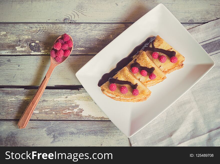 Crepes with fresh raspberries and chocolate syrop on aged wooden background. Top view. Crepes with fresh raspberries and chocolate syrop on aged wooden background. Top view.