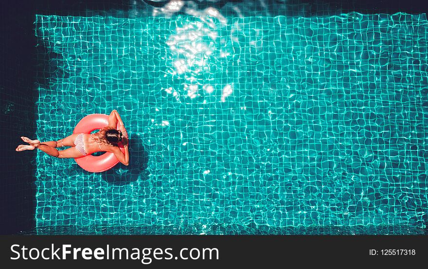 Young pretty slim woman in straw hat on a pink air mattress in t