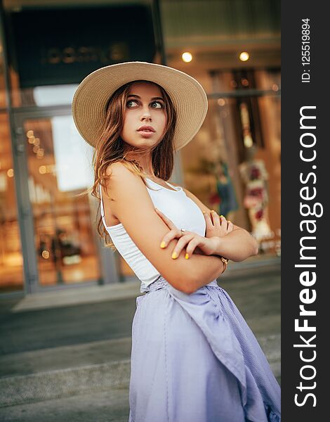 Young woman in hat stands at city street on background of building. Young woman in hat stands at city street on background of building.